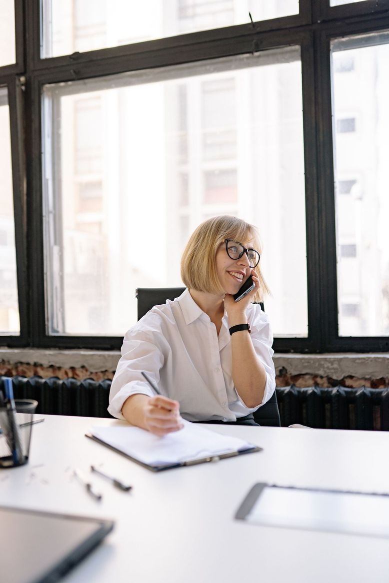 An account manager taking a client call at their desk, making notes.